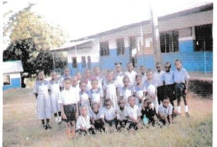 Pupils of KAG School in uniform, gathered on the grass in front of a classroom block