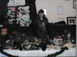 Dim photo of a woman standing behind a long table of goods in a hall, with pictures on the wall behind