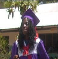 A girl with long braids wearing a purple graduation gown and cap outside a school building