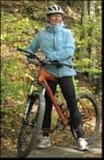 A woman in a blue jacket and cycling helmet standing with a mountain bike on a woodland path
