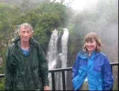 A man and a woman in rain jackets standing at a railing in front of a tall waterfall