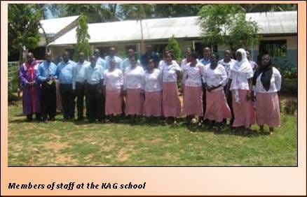 KAG School staff in uniform standing in a row on the grass in front of a classroom block