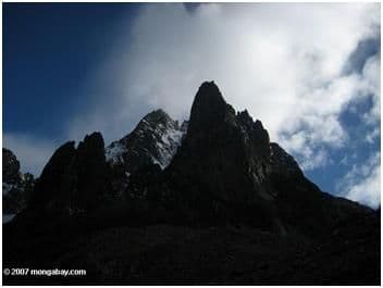 Jagged dark peaks of Mount Kenya against a blue sky with clouds