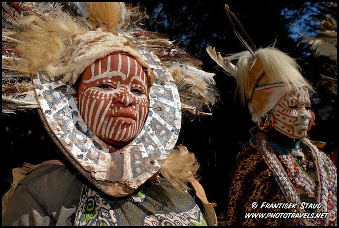 Two women with red and white painted faces wearing feathered traditional headdresses