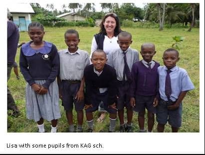 A visiting woman standing on a school field with a group of KAG pupils in uniform