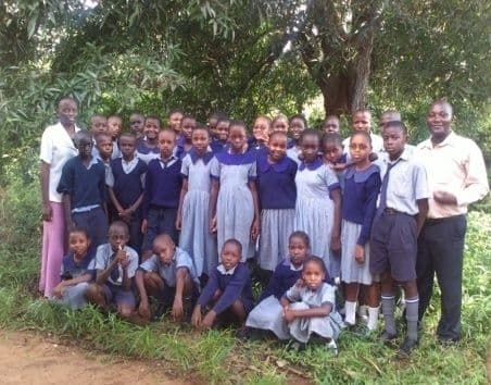 Bible club members in uniform standing and kneeling in rows outdoors with two teachers