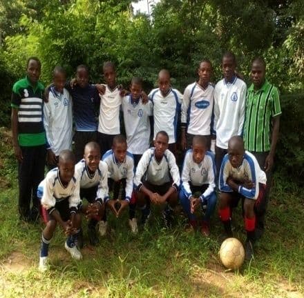 The school football team in white and blue kit posing in two rows with a ball