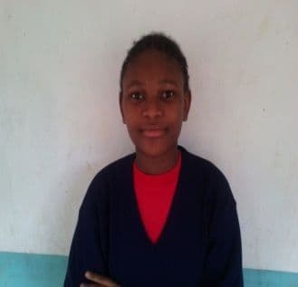 Head-and-shoulders portrait of a schoolgirl in a navy jumper against a white wall