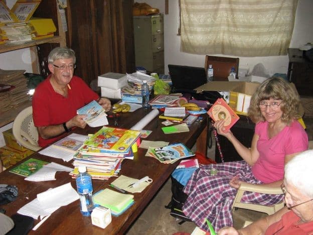 Two visiting women at a table covering and cataloguing children's books in the library