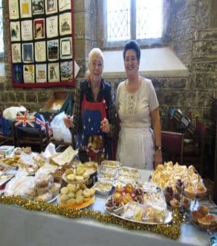 Two women behind a table of home baking at the fayre