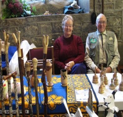A man and a woman seated at a stall of carved walking sticks and wooden animals
