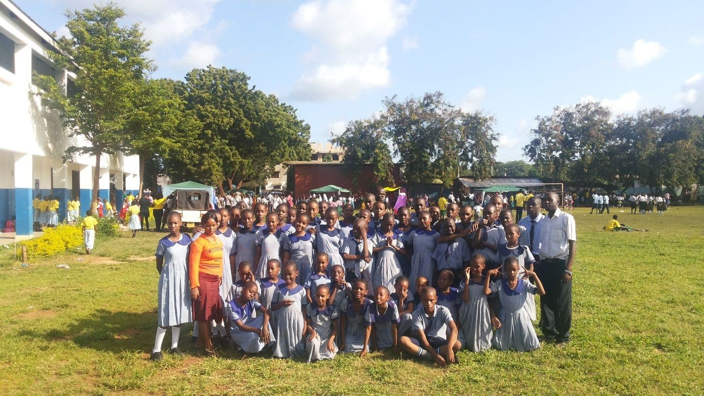 A large group of pupils and teachers posing on a grass field in front of school buildings