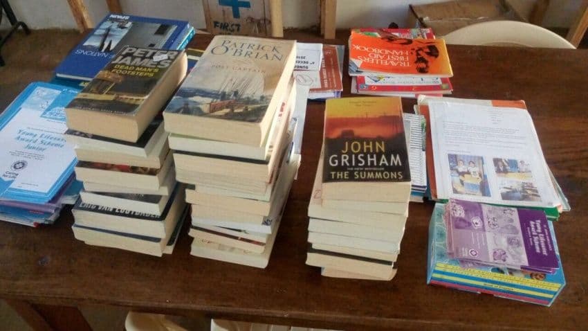 Piles of donated paperback novels and reference books spread across a wooden table