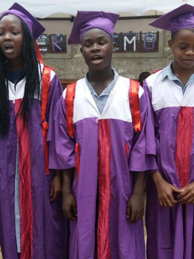 Three pupils in purple and white graduation gowns and mortarboards singing outdoors