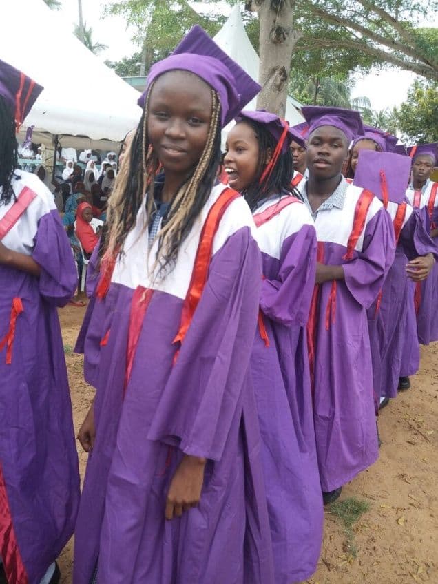 Line of pupils in purple graduation gowns and caps queuing outside