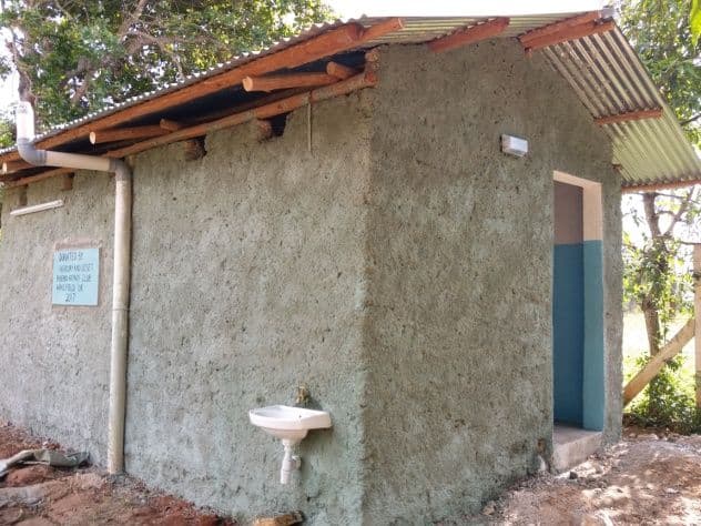 Side view of a new cement-plastered toilet block with a corrugated roof and outdoor hand basin