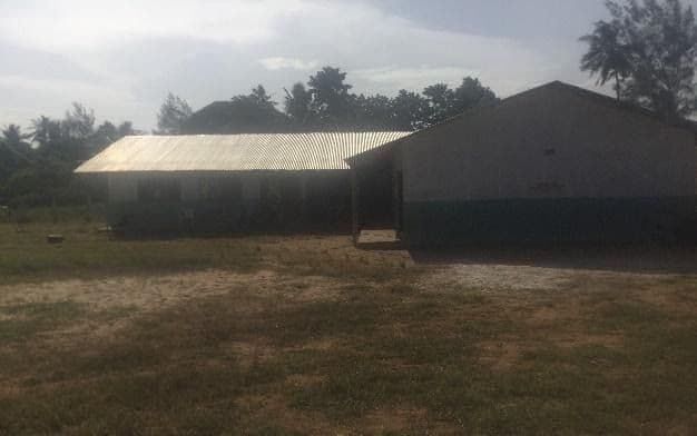 Single-storey classroom block with a corrugated roof beside a grassy field