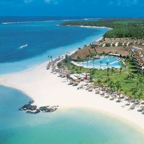 Aerial view of a white sand beach and turquoise sea beside a resort with a pool and palms