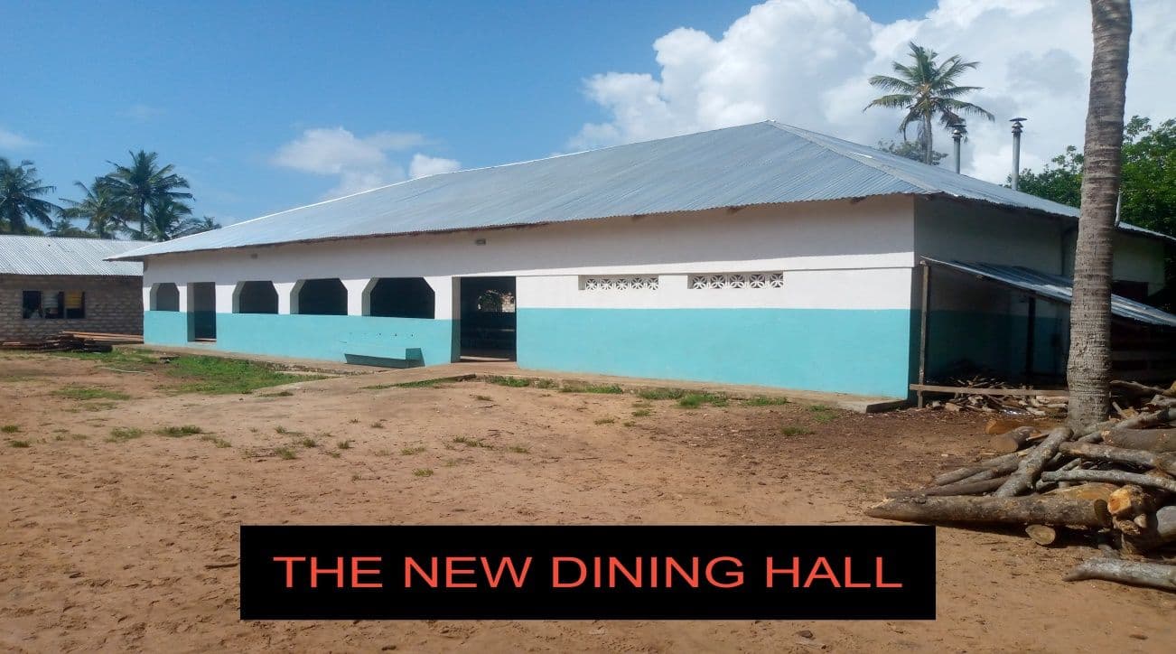 Newly built single-storey dining hall with white and turquoise walls and an iron roof, palm trees behind