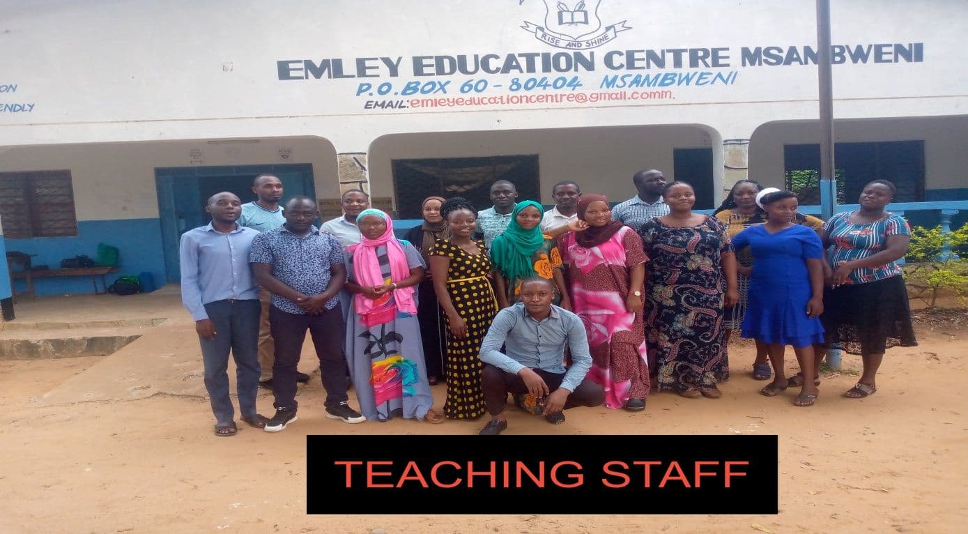 Group of teachers standing and crouching in front of the Emley Education Centre building