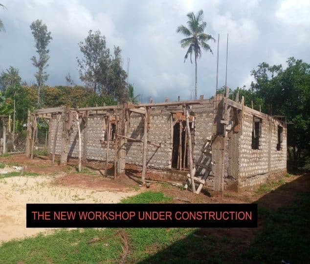 A stone building with timber scaffolding and roof frame under construction among palm trees