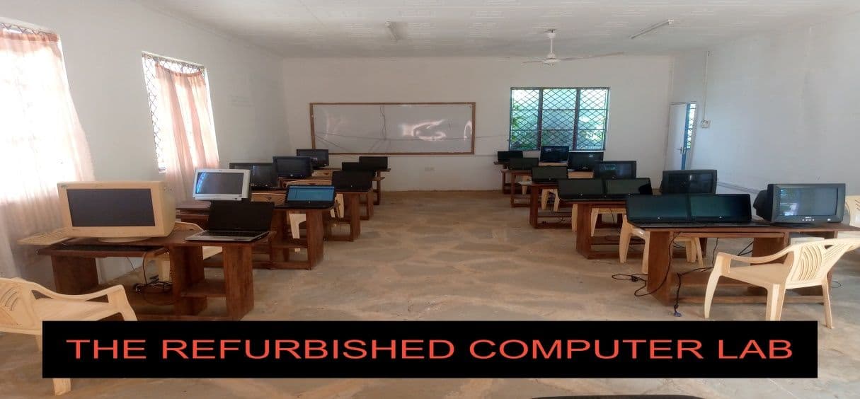 Computer room with rows of laptops and desktop monitors on wooden desks and plastic chairs