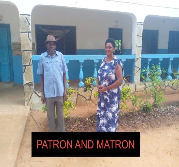 A man in a hat and a woman in a blue dress standing outside a school building