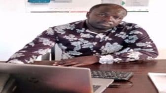 Man in a patterned shirt seated at a desk with a laptop