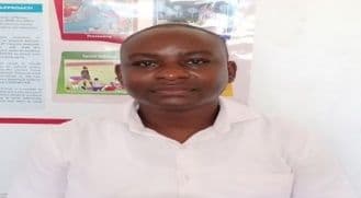 Man in a white shirt in front of a classroom wall with posters