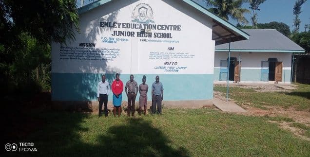 Five staff members standing in front of the Emley Education Centre Junior High School building