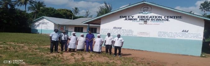 Support staff, some in white cook's coats, standing outside the Junior High School building