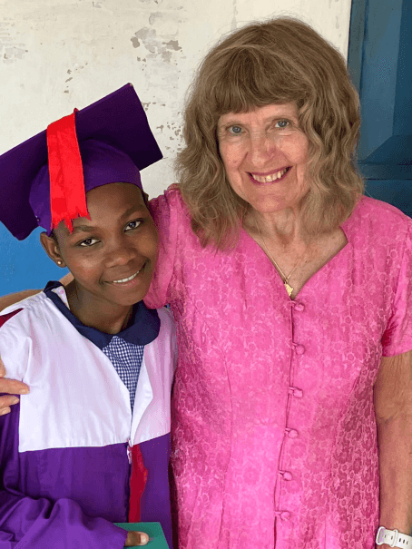 Pupil in a purple graduation gown and mortarboard standing beside a smiling woman in a pink dress