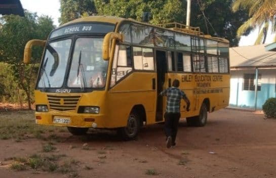 Yellow Emley Education Centre school bus parked on red earth under trees, a man walking toward its door