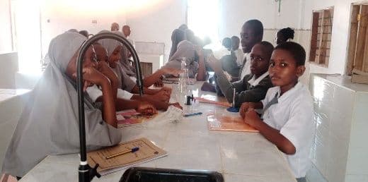 Students in uniform seated at white lab benches with taps and worksheets in the science laboratory