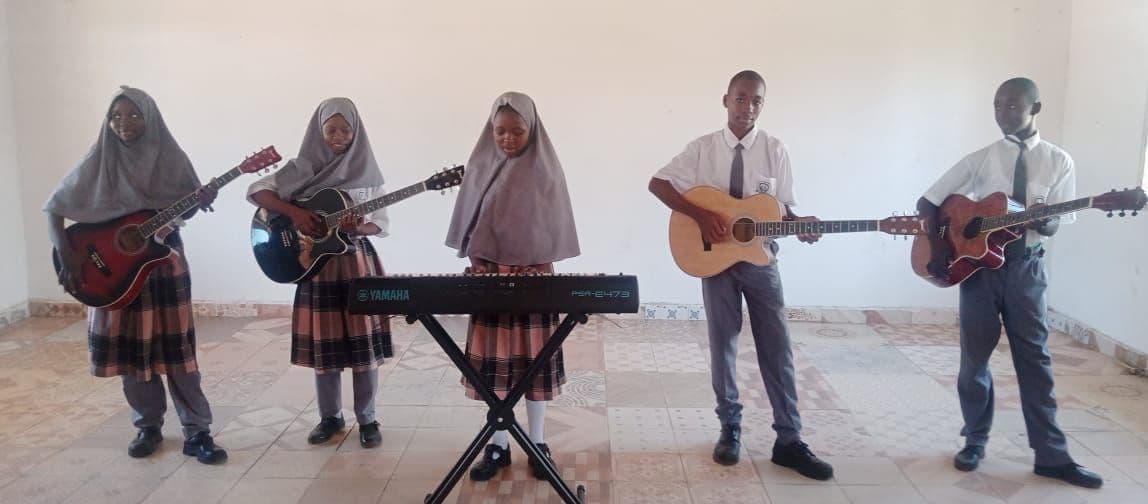 Five students in uniform playing acoustic guitars and an electronic keyboard in a classroom