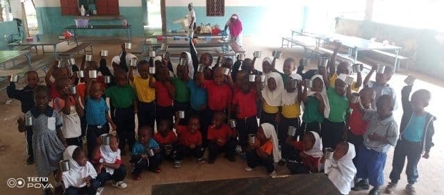 Large group of young children raising cups in the air inside the dining hall
