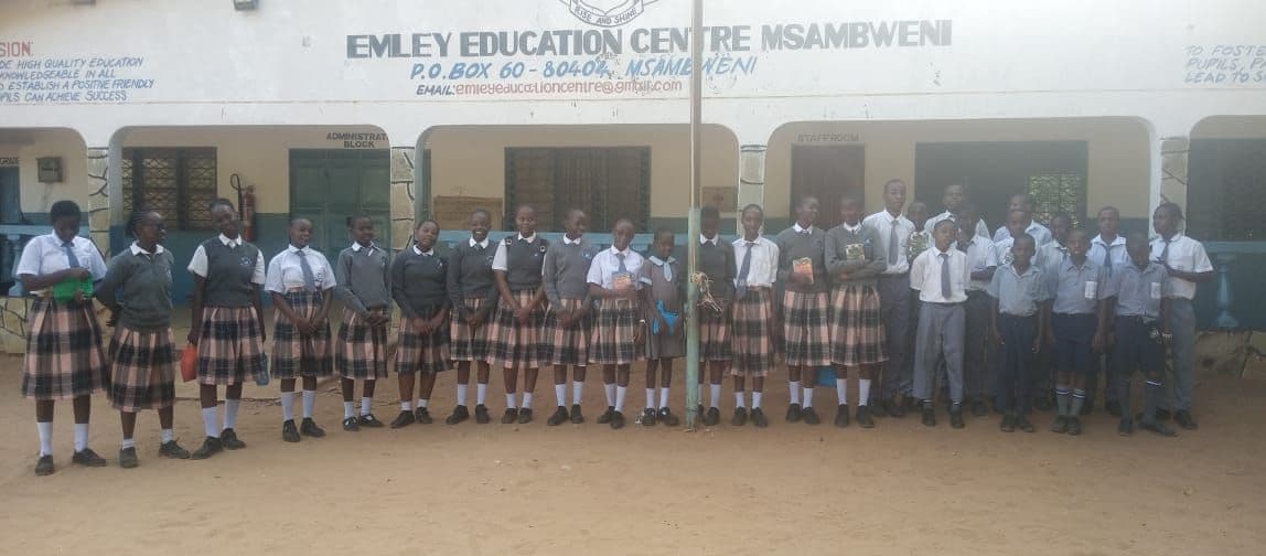 Students in grey uniforms standing in a line in front of the school administration block