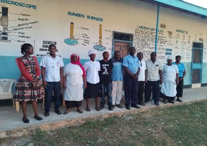 Support staff, including cooks in white aprons and caps, standing in a line outside the science lab