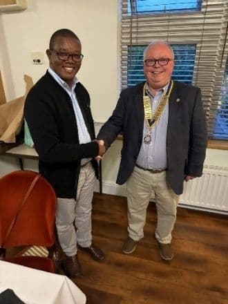 Two men shaking hands indoors, one wearing a Rotary chain of office