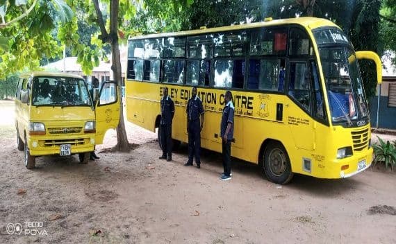 Yellow Emley Education Centre school bus and van parked on sand, with three uniformed staff beside the bus