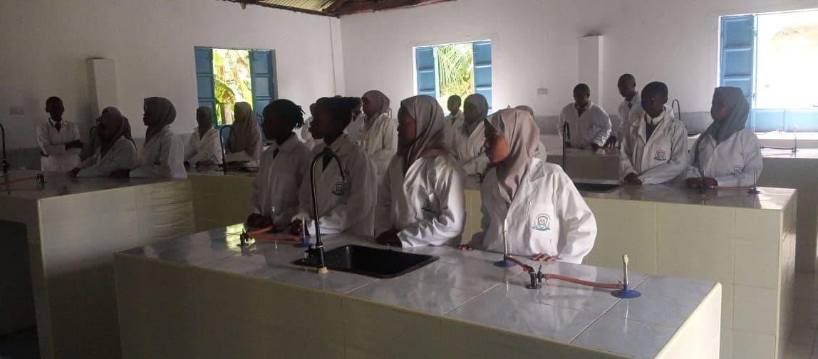 Students in white lab coats standing at tiled benches with sinks and gas taps in the science laboratory