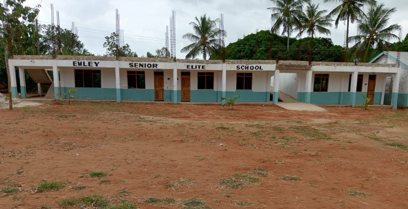 New single-storey classroom block signed Emley Senior Elite School, with palm trees behind