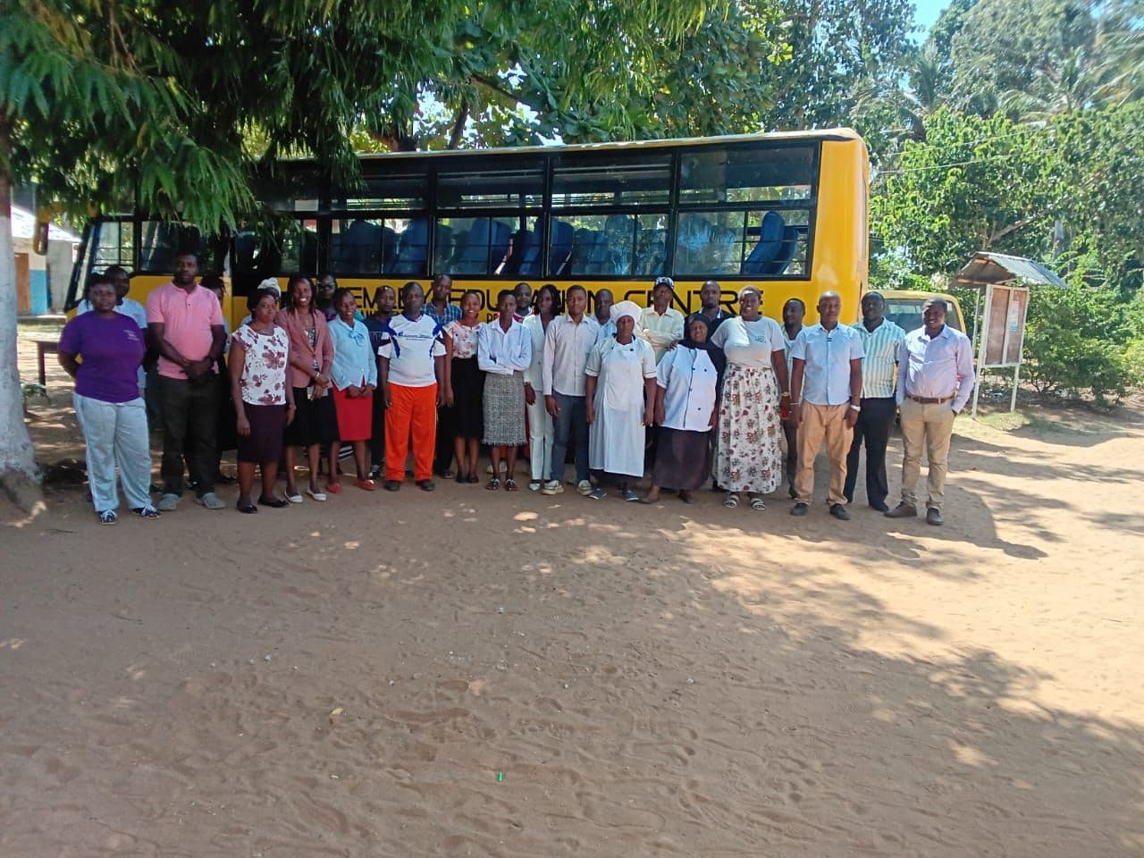 School staff standing in a line outdoors in front of a yellow school bus