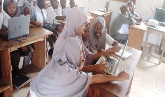 Learners in headscarves working on laptops at wooden desks in the computer lab