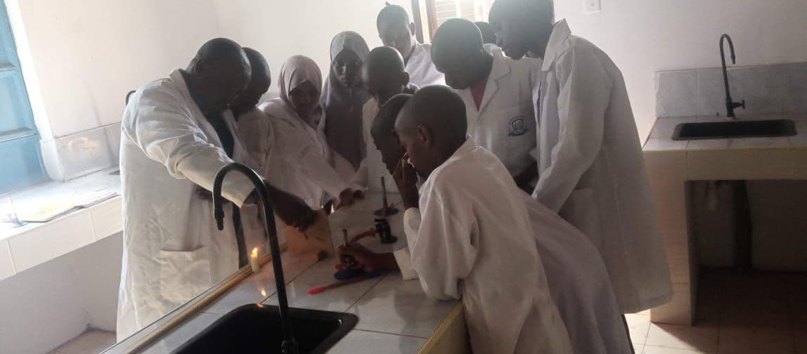 Learners in white lab coats gathered around a bench doing an experiment in the science laboratory