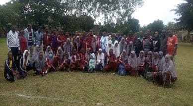 Large group of learners in maroon tracksuits and teachers posing on a grass field