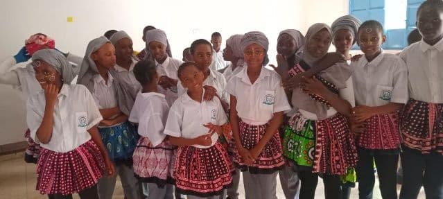 Girls in white blouses and red patterned skirts standing together in a classroom