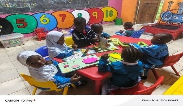 Young children playing with toys at small red tables in a colourful daycare classroom