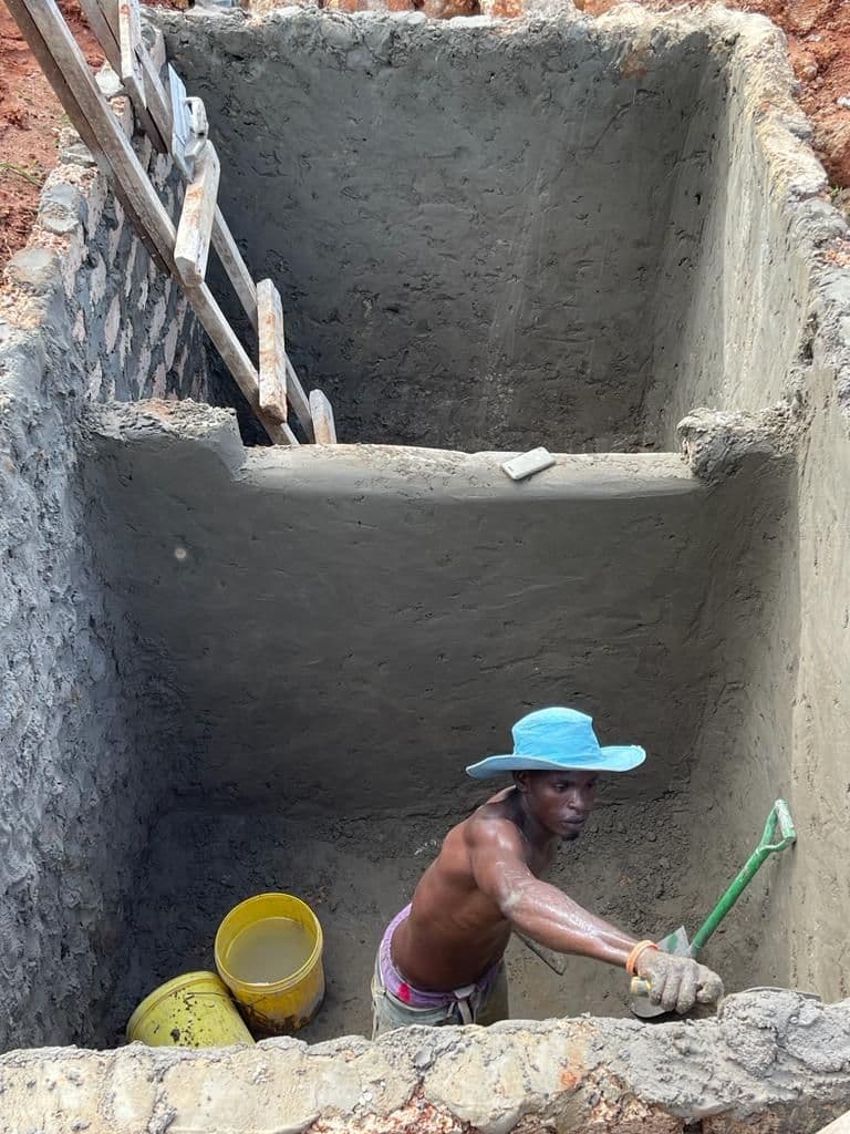 A builder in a blue hat plastering the inside walls of a new concrete septic tank