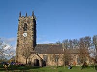 Stone parish church with a square clock tower, seen across a lawn under a blue sky